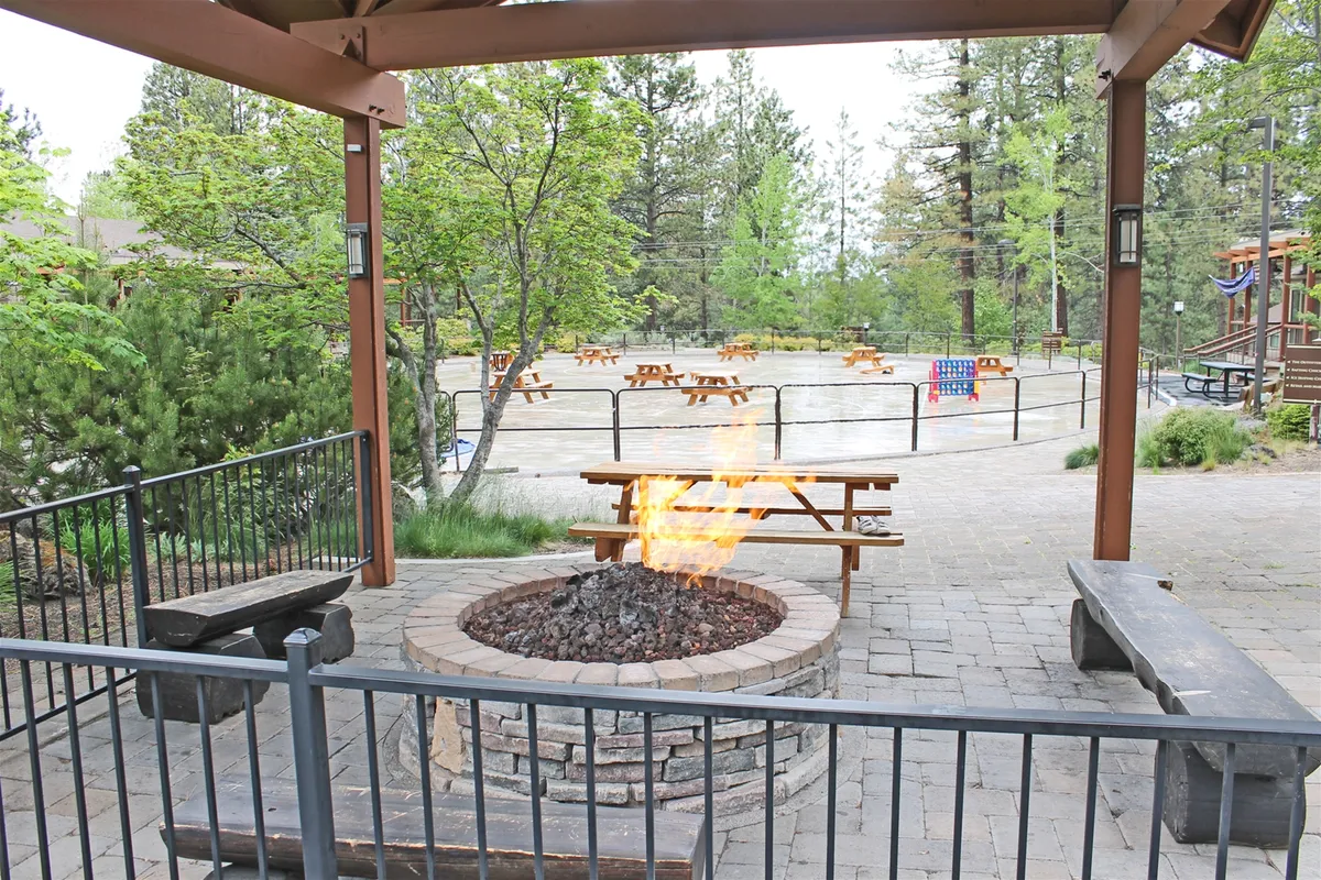 An inviting fire pit sits among picnic tables and lush greenery, providing a perfect gathering spot for guests to enjoy s'mores, conversation, and casual outdoor games as the sun sets.