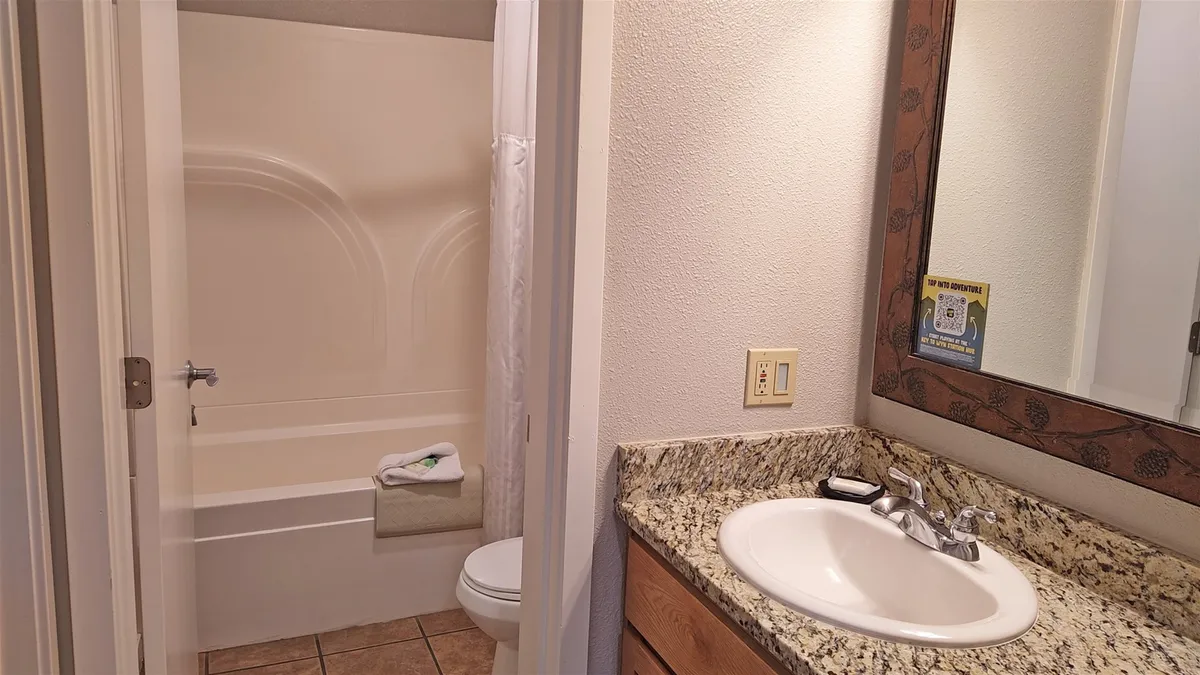 A bright and well-equipped bathroom with a granite countertop, elegant sink, deep bathtub, and a large mirror. The space is clean and modern, balancing both functionality and relaxation.