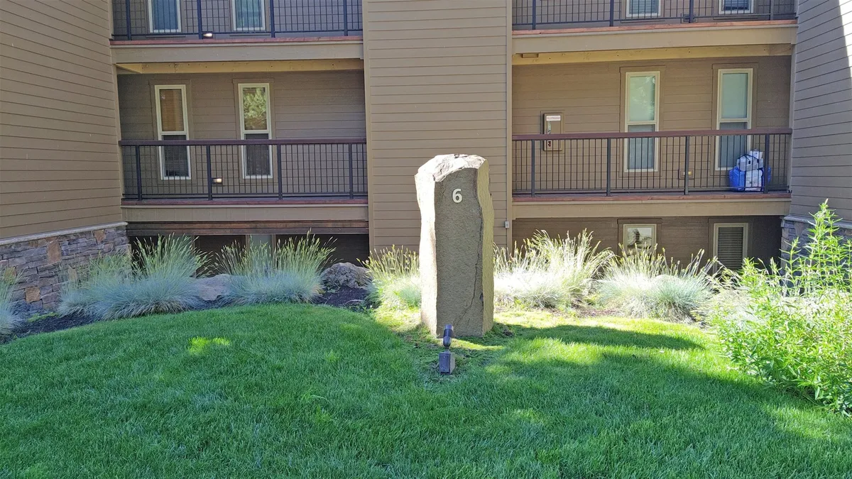 A lush green lawn with a stone marker and surrounding vegetation provides a serene backdrop. The view hints at the type of greenery one might see from a balcony and evokes the peaceful, inviting mood described in the section.