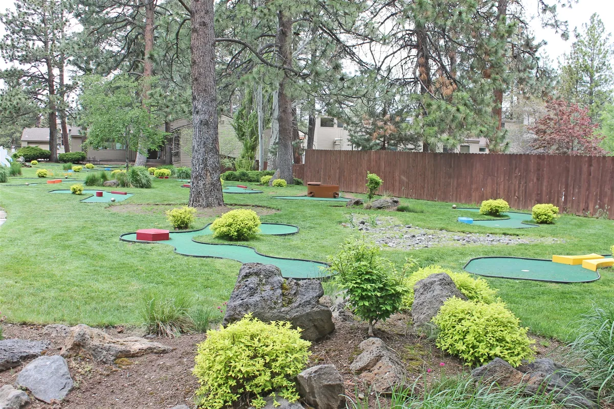 A vibrant mini-golf course winds through lush greenery and natural rock formations, dotted with colorful obstacles. The scene buzzes with a joyful, playful mood and invites families or friends to enjoy a casual, fun activity in the sunshine.
