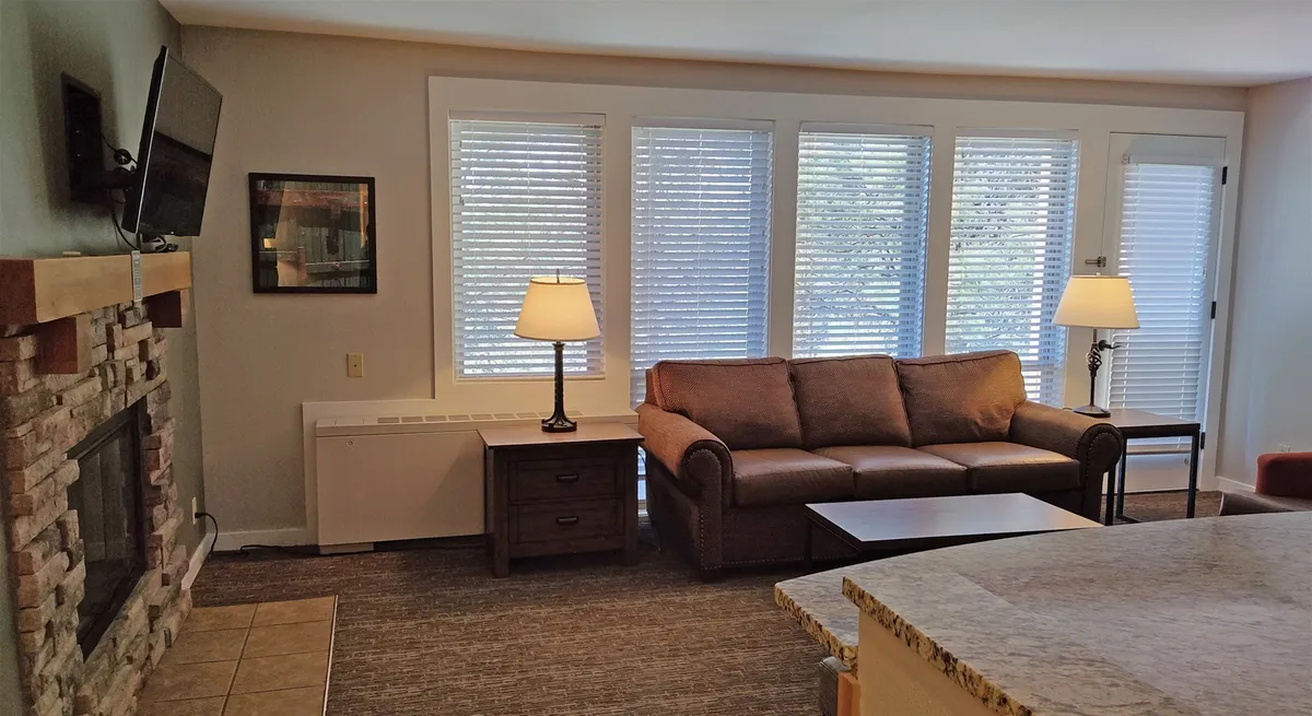 A cozy living area featuring a comfortable sofa, a glowing fireplace, and a large window that fills the space with natural light. The arrangement is inviting for both relaxation and socializing, with warm lighting and a welcoming atmosphere.