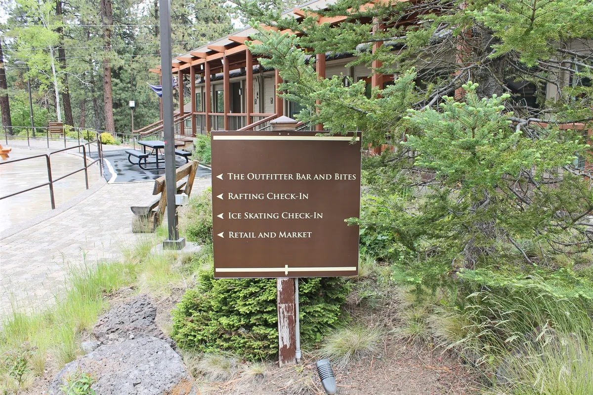 This image shows a welcoming signpost at the resort, surrounded by lush greenery and a glimpse of the building structure. The atmosphere is lively and hints at nearby action, with signage likely pointing to activities like rafting, ice skating, and dining.