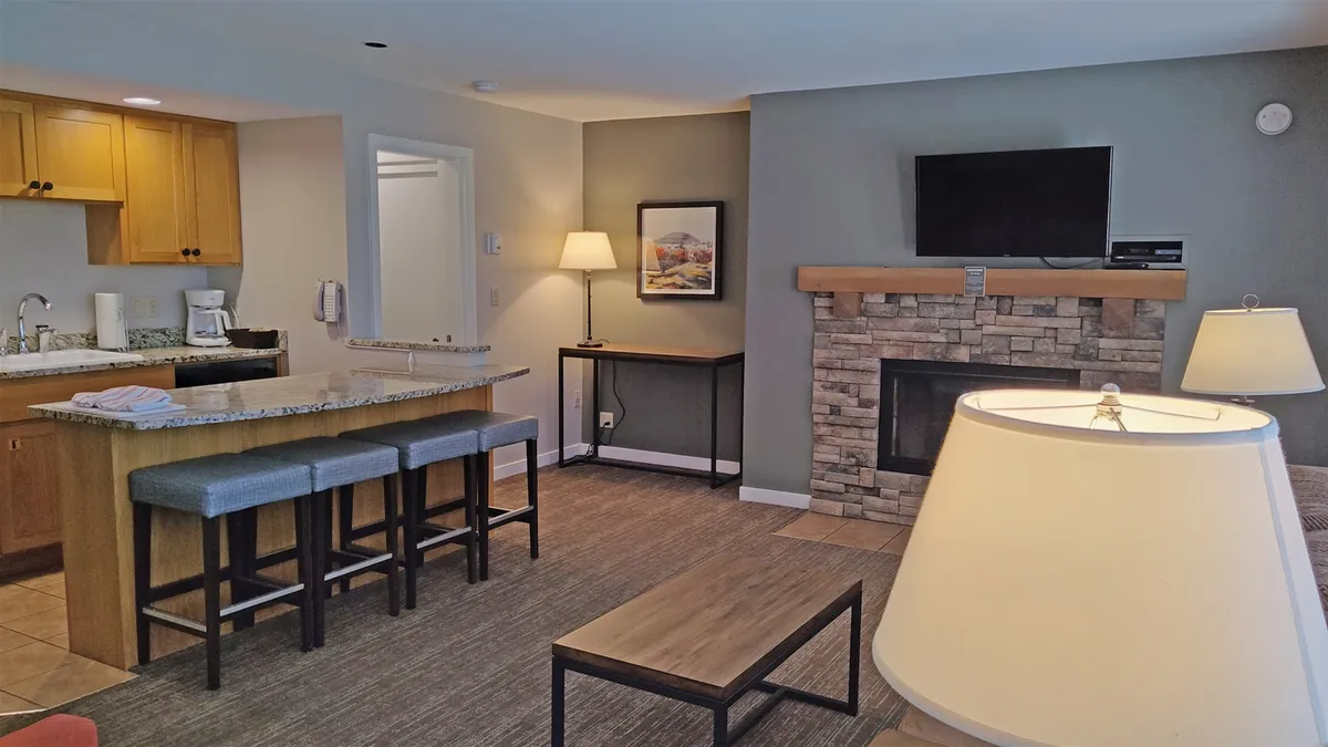 A wide view of the open-concept living area, seamlessly connecting a modern kitchen, a comfortable seating area, a coffee table, and a fireplace. The arrangement is conducive to socializing, dining, and relaxing—all in one communal space.