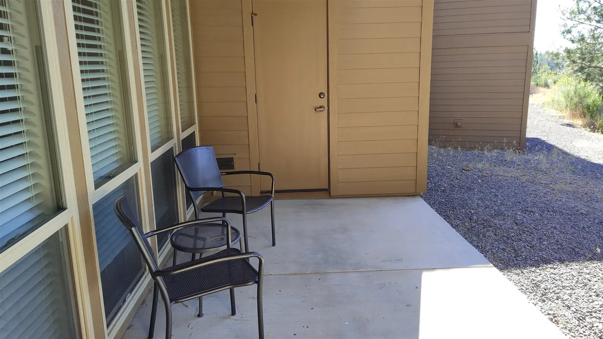 This image features two black chairs positioned outside a front door, flanked by large windows. The chairs are situated in a peaceful, sunlit area, suggesting a perfect spot for morning coffee or quiet relaxation. The ground-level perspective highlights accessibility and ease of use for both pets and children.